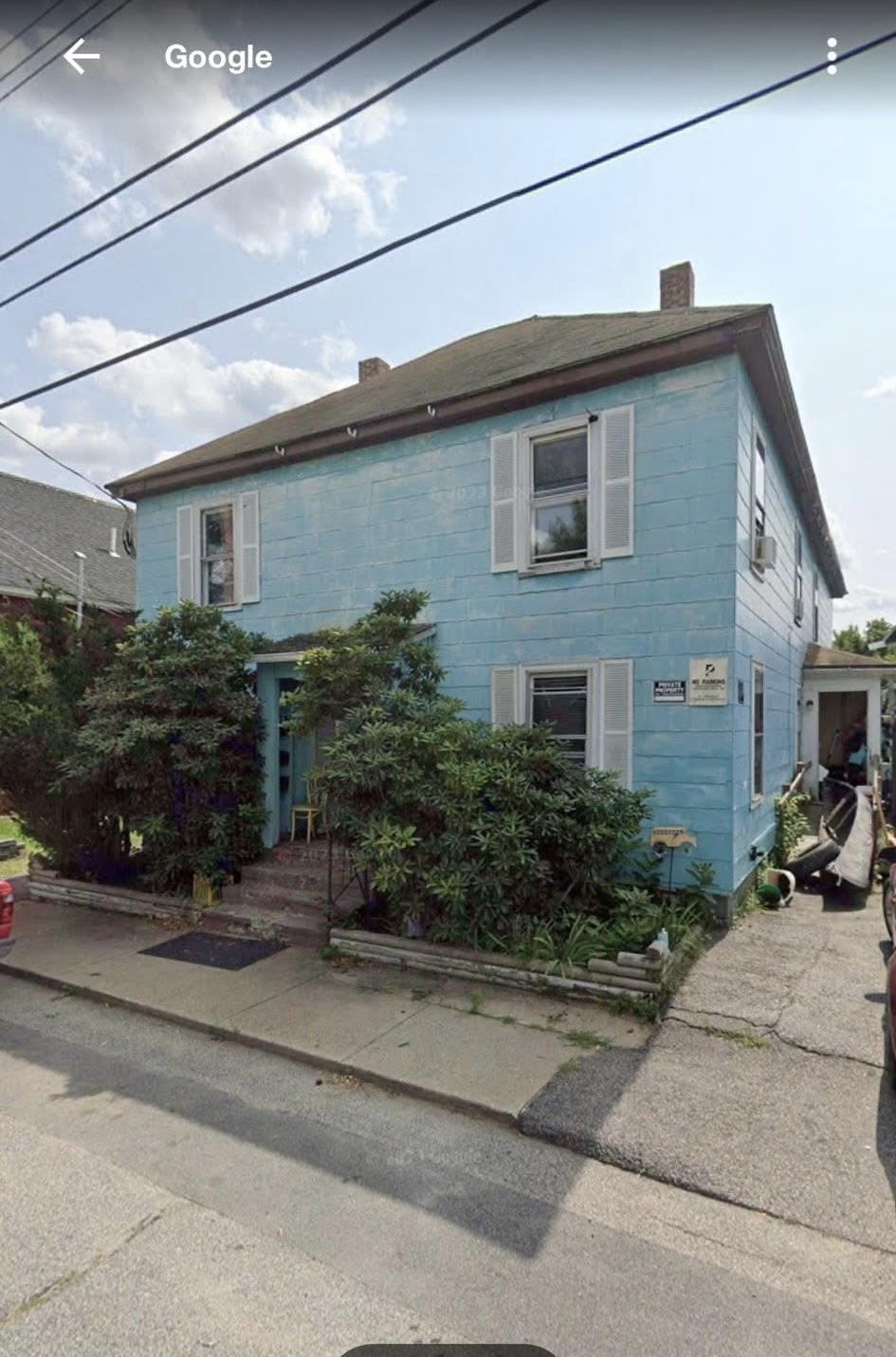 Two-story home with weathered blue siding and overgrown shrubs before renovation