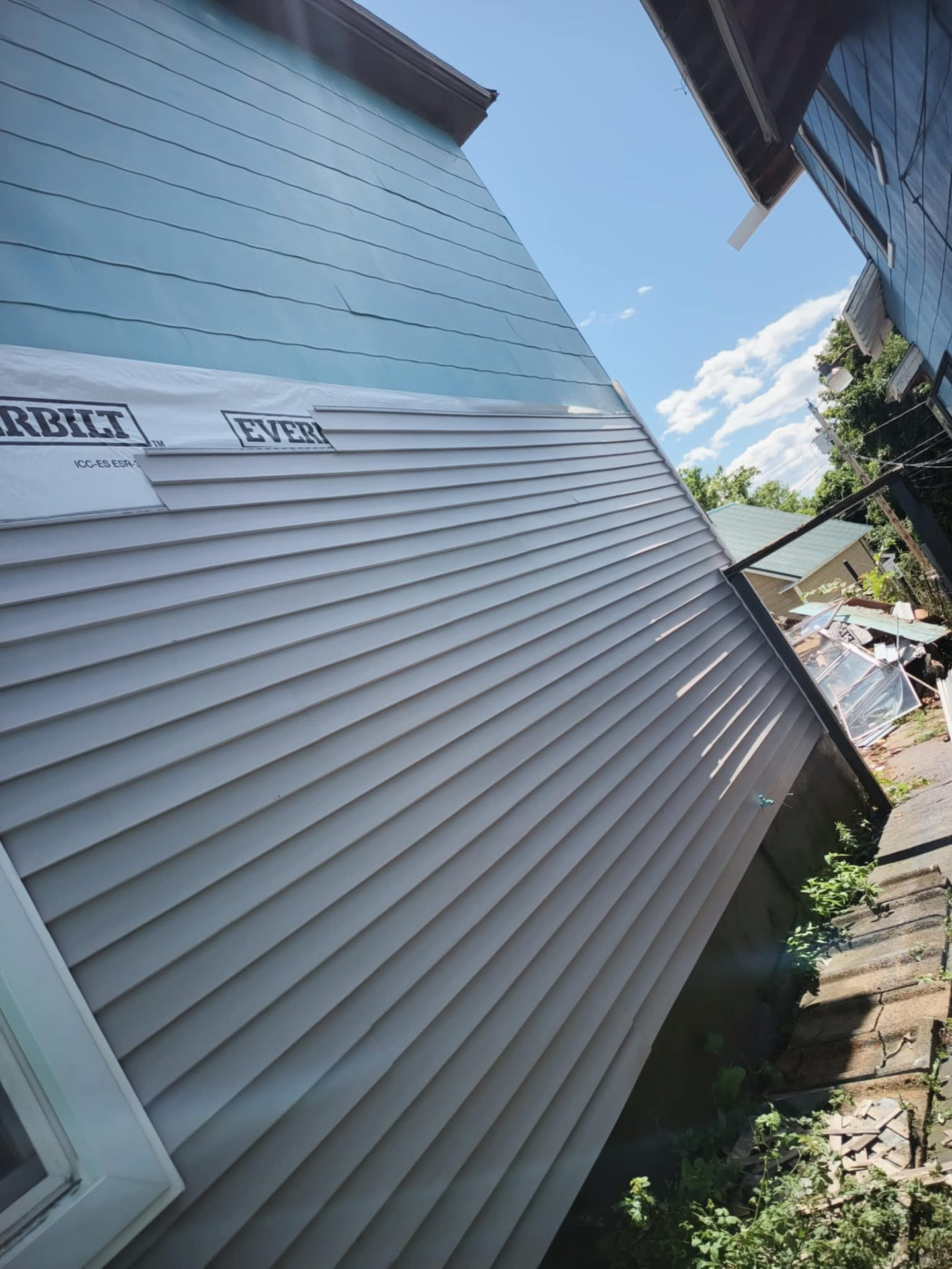 Siding installation in progress with house wrap visible