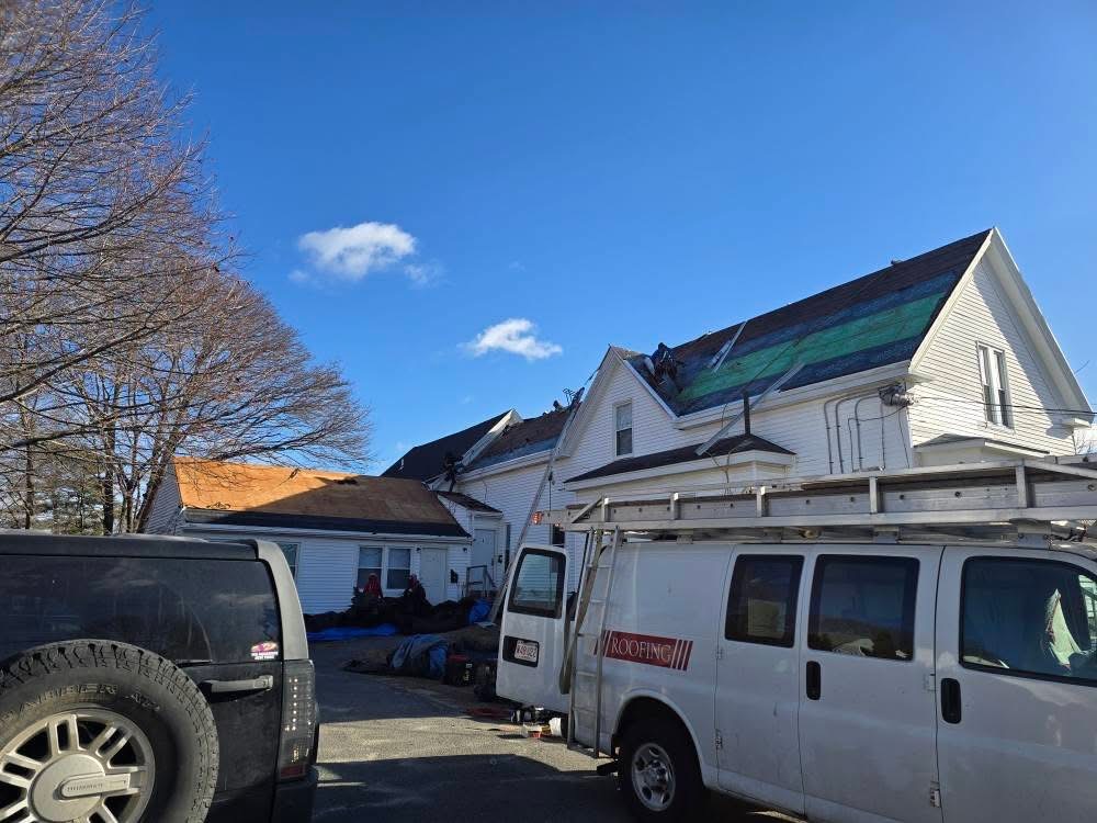 Roof mid tear-off with exposed decking and underlayment, crew and van on site